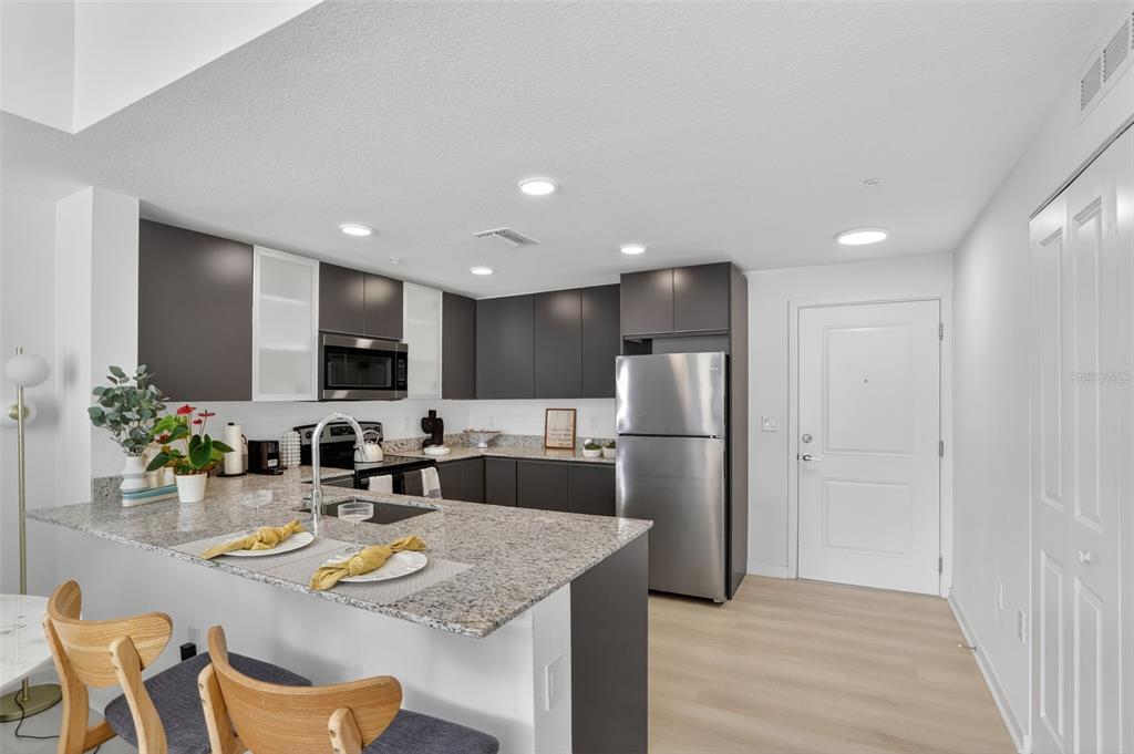 A modern kitchen features dark cabinetry, granite countertops, stainless steel appliances, and a breakfast bar — 5579 MILLENIA PARK BOULEVARD UNIT 523, ORLANDO, FL