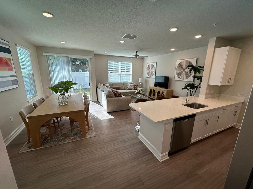 An open-concept kitchen, dining area, and living room featuring light wood flooring and white cabinetry — 1057 E CAROLINE STREET, TAVARES, FL