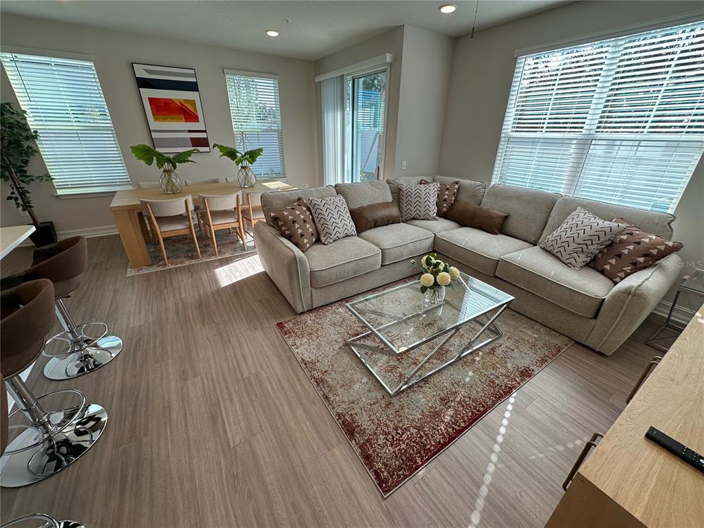 A living room and dining area feature light wood flooring, a sectional sofa, and windows — 1057 E CAROLINE STREET, TAVARES, FL