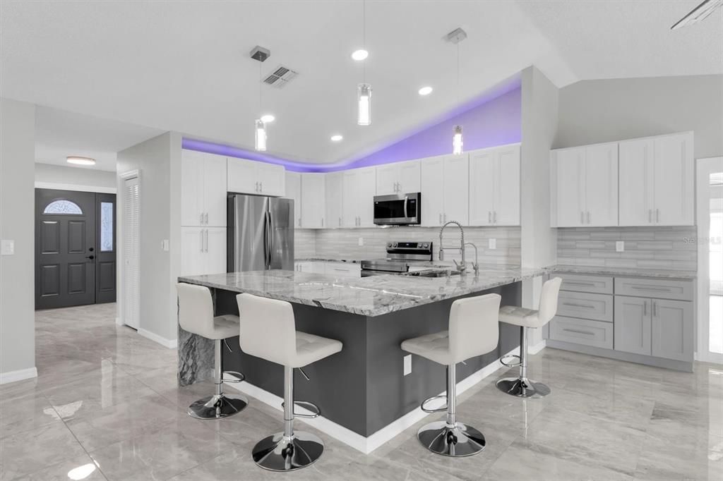 A modern kitchen features a gray island with bar stools, white cabinetry, and purple accent lighting — 8345 APPLE ORCHARD ROAD, SPRING HILL, FL