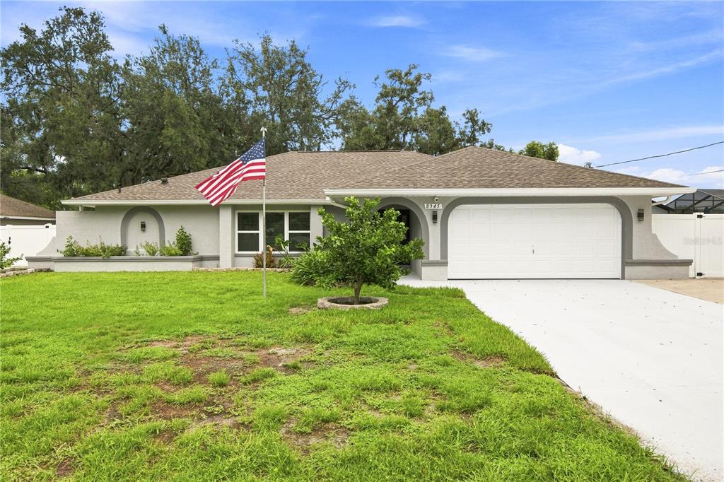A backyard view of a single-story house with a large lawn and two mature trees — 8345 APPLE ORCHARD ROAD, SPRING HILL, FL