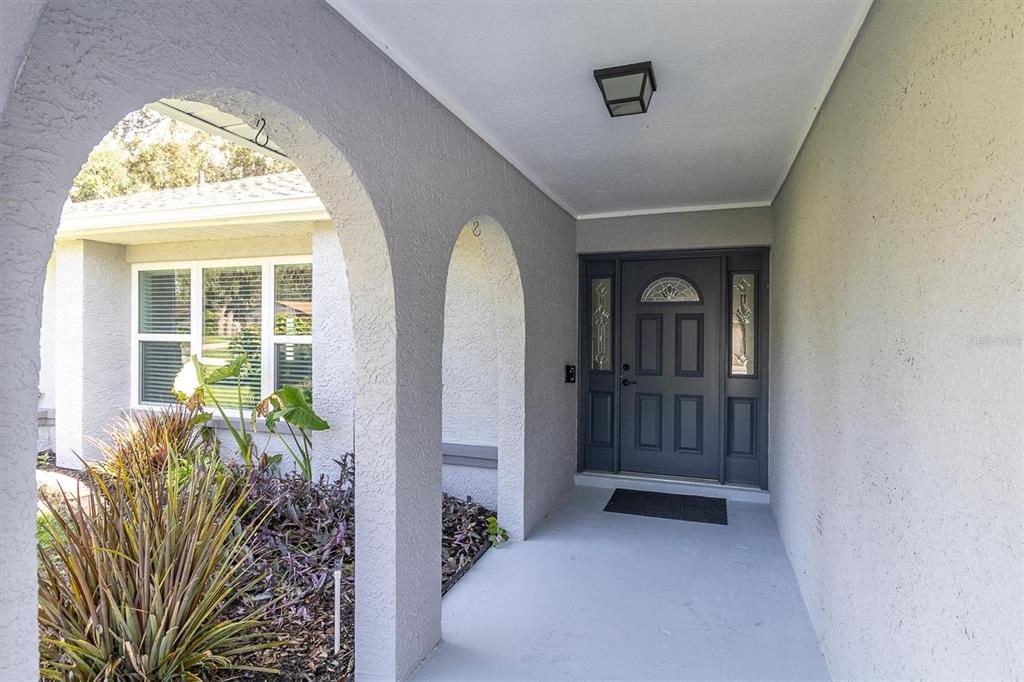 A covered entryway features a gray front door with sidelights and arched stucco columns — 8345 APPLE ORCHARD ROAD, SPRING HILL, FL