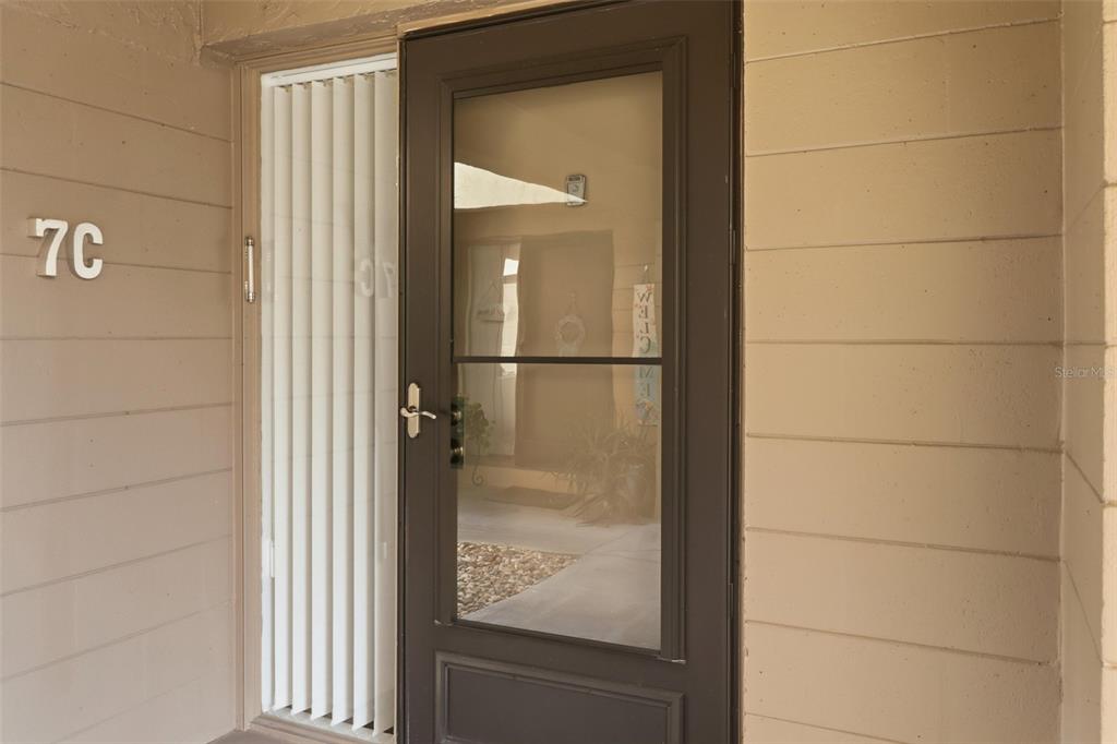 A brown storm door with a glass panel is mounted on a beige exterior wall — 130 JASMINE WOODS COURT UNIT 7C, DELTONA, FL