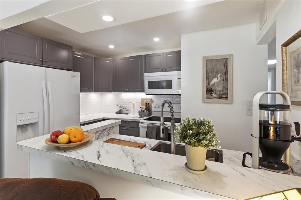 A kitchen features gray cabinets, white marble-look countertops, a white refrigerator, and a breakfast bar — 130 JASMINE WOODS COURT UNIT 7C, DELTONA, FL