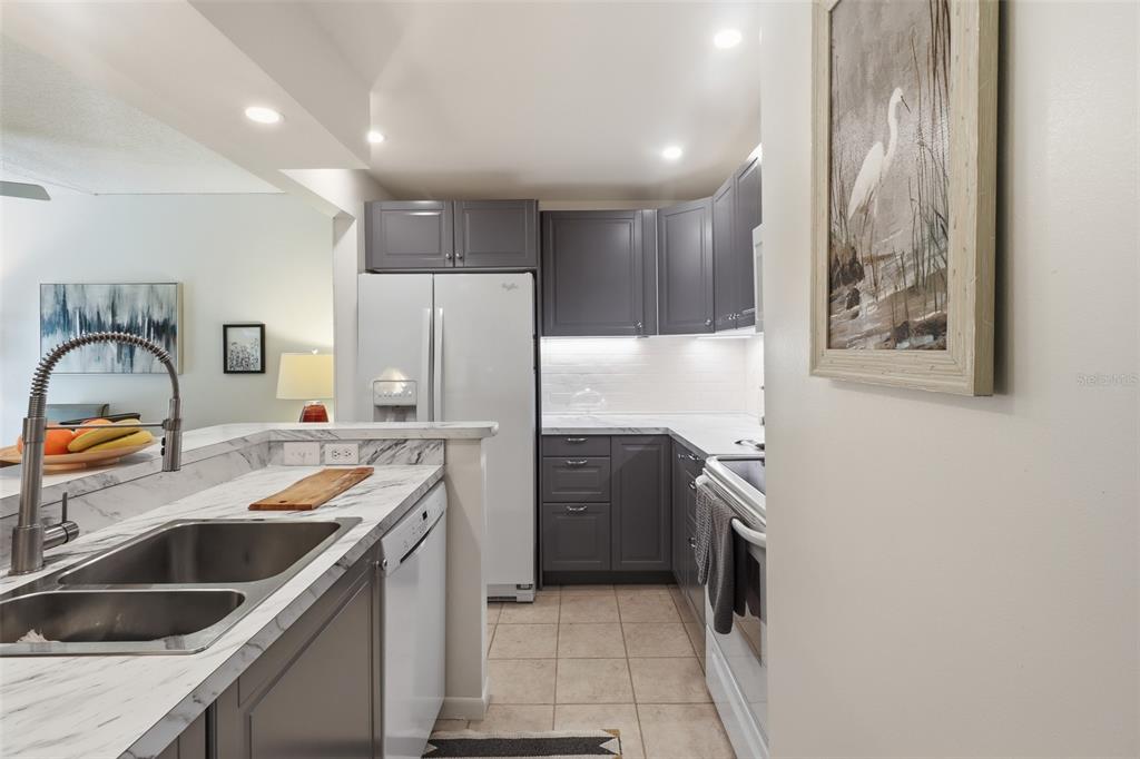 A kitchen features gray cabinets, white countertops, a double sink, and white appliances — 130 JASMINE WOODS COURT UNIT 7C, DELTONA, FL