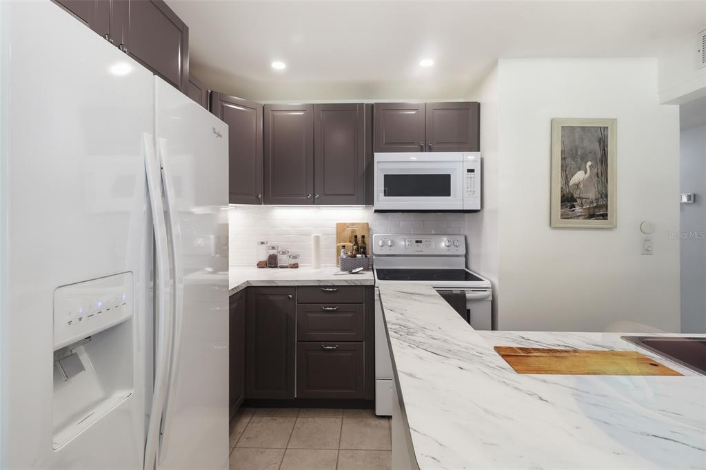 A kitchen features dark gray cabinets, white marble-look countertops, and a white refrigerator — 130 JASMINE WOODS COURT UNIT 7C, DELTONA, FL