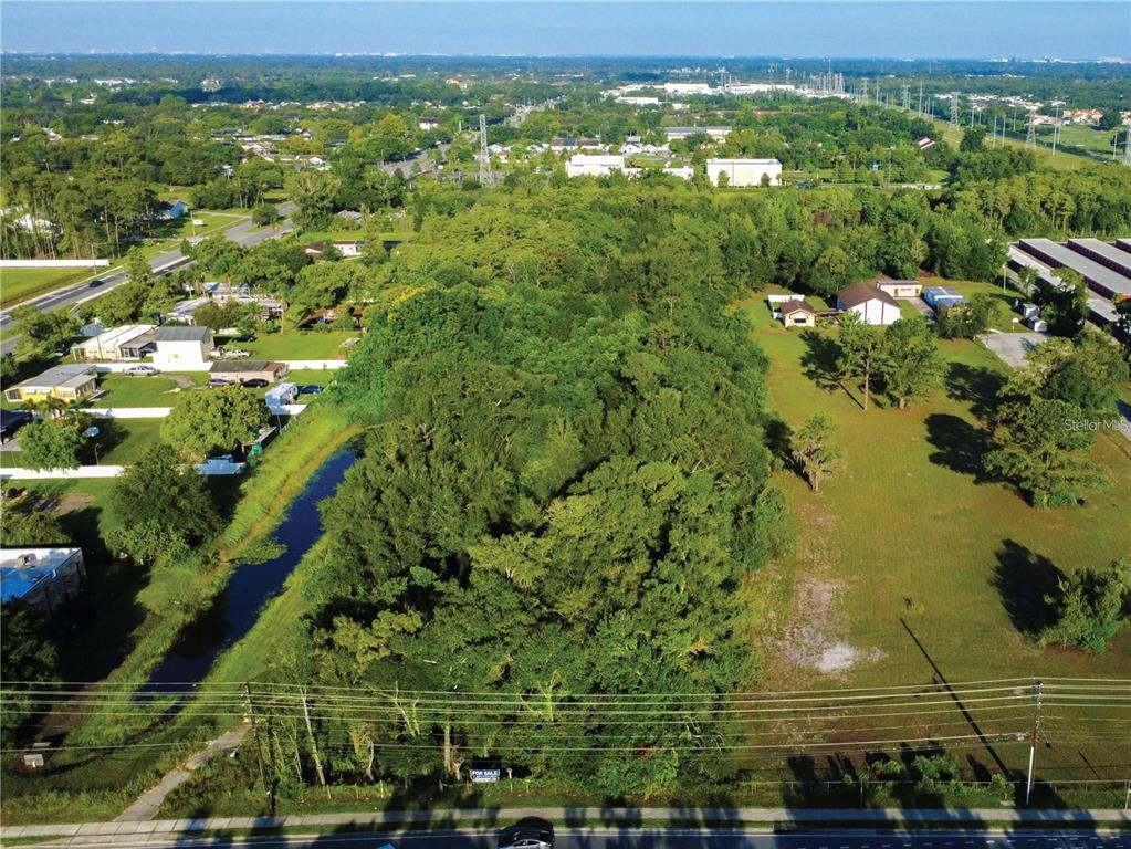 An aerial view shows a large, wooded vacant lot bordered by a road and residential buildings — 3106 S GOLDENROD ROAD, ORLANDO, FL