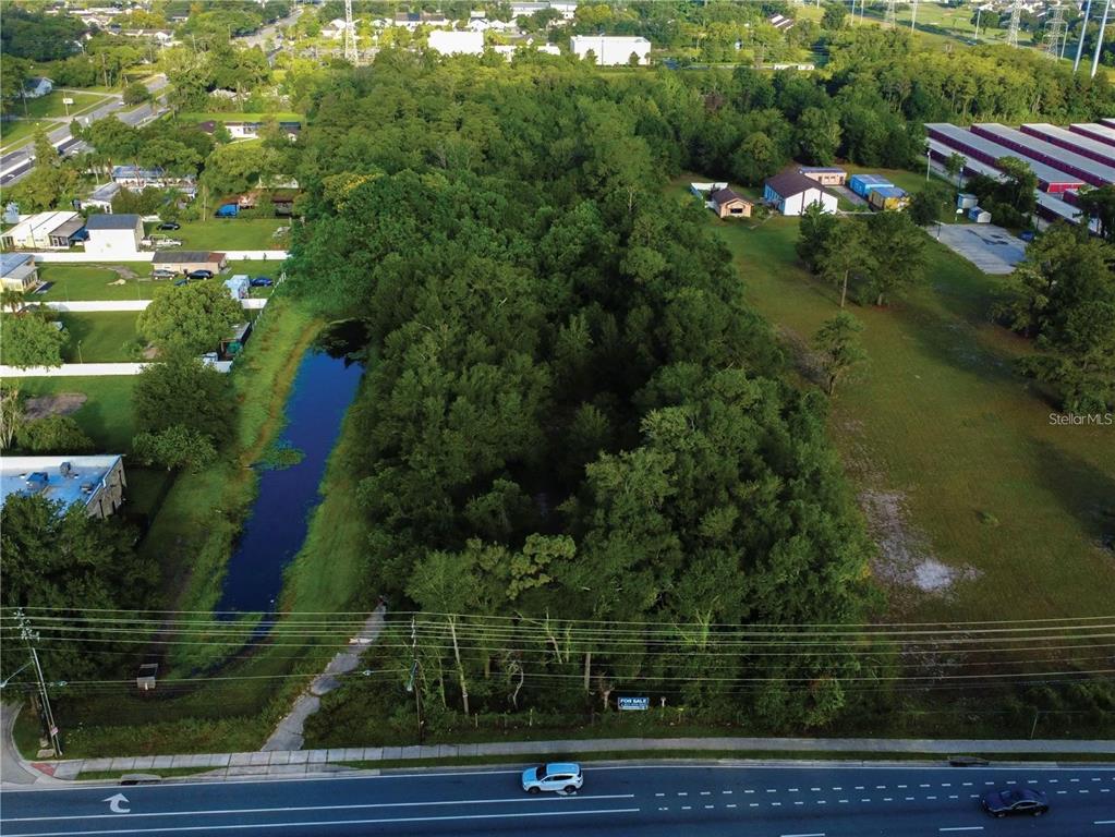 An aerial view shows a wooded lot with a pond next to a multi-lane road — 3106 S GOLDENROD ROAD, ORLANDO, FL