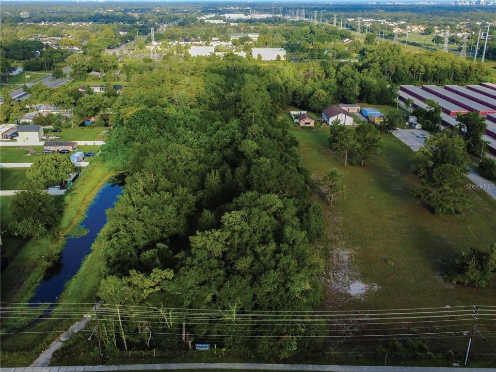 An aerial view shows a wooded lot adjacent to a canal and a grassy field — 3106 S GOLDENROD ROAD, ORLANDO, FL