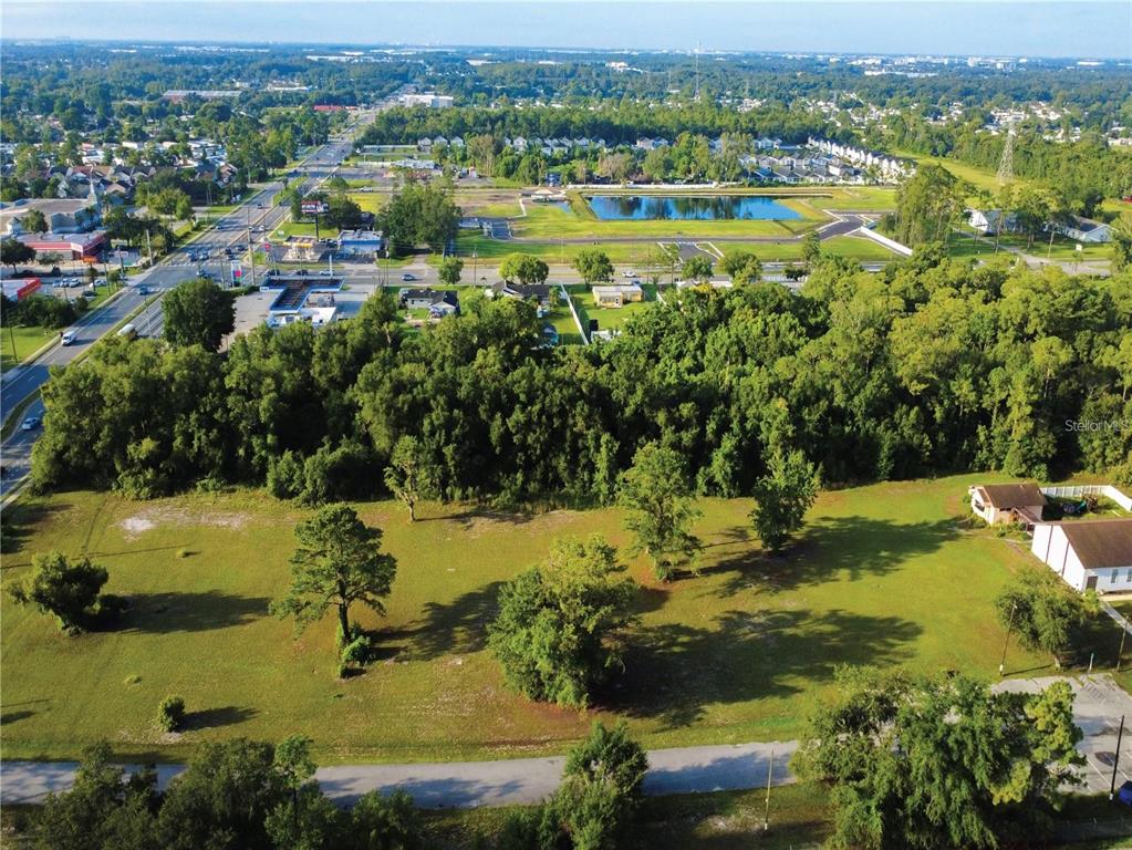 An aerial view shows a large, grassy vacant lot bordered by trees and nearby roads — 3106 S GOLDENROD ROAD, ORLANDO, FL