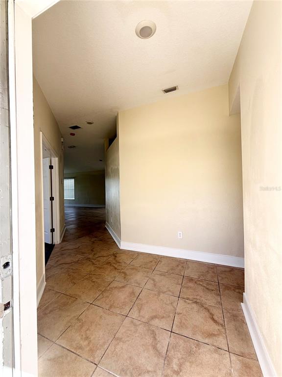 An entryway with tan tile flooring leads into a hallway with beige walls — 7731 CARRIAGE POINTE DRIVE, GIBSONTON, FL