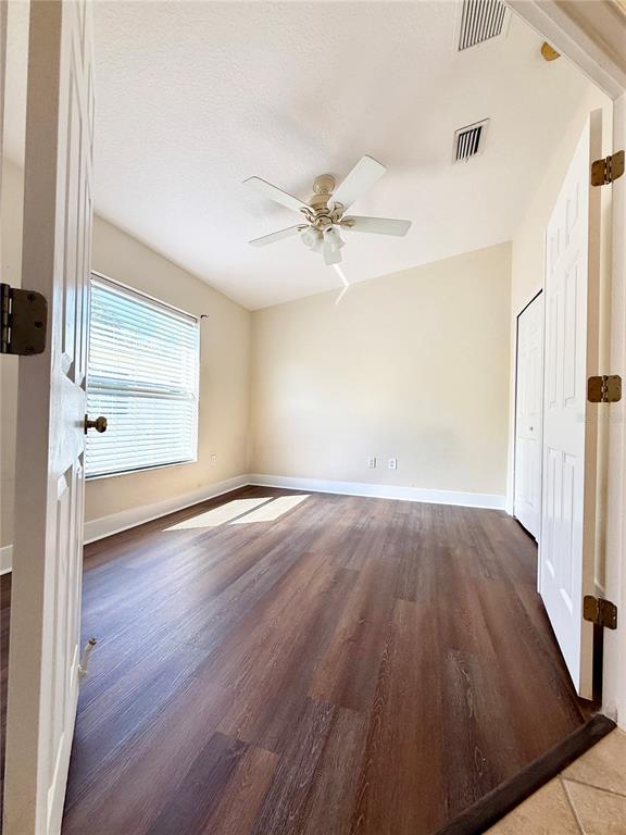 An empty bedroom features dark wood-look flooring, a ceiling fan, and a window with blinds — 7731 CARRIAGE POINTE DRIVE, GIBSONTON, FL