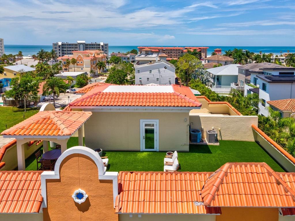 An elevated view of a rooftop terrace with artificial turf, patio furniture, and tiled roofs — 138 175TH AVENUE E, REDINGTON SHORES, FL