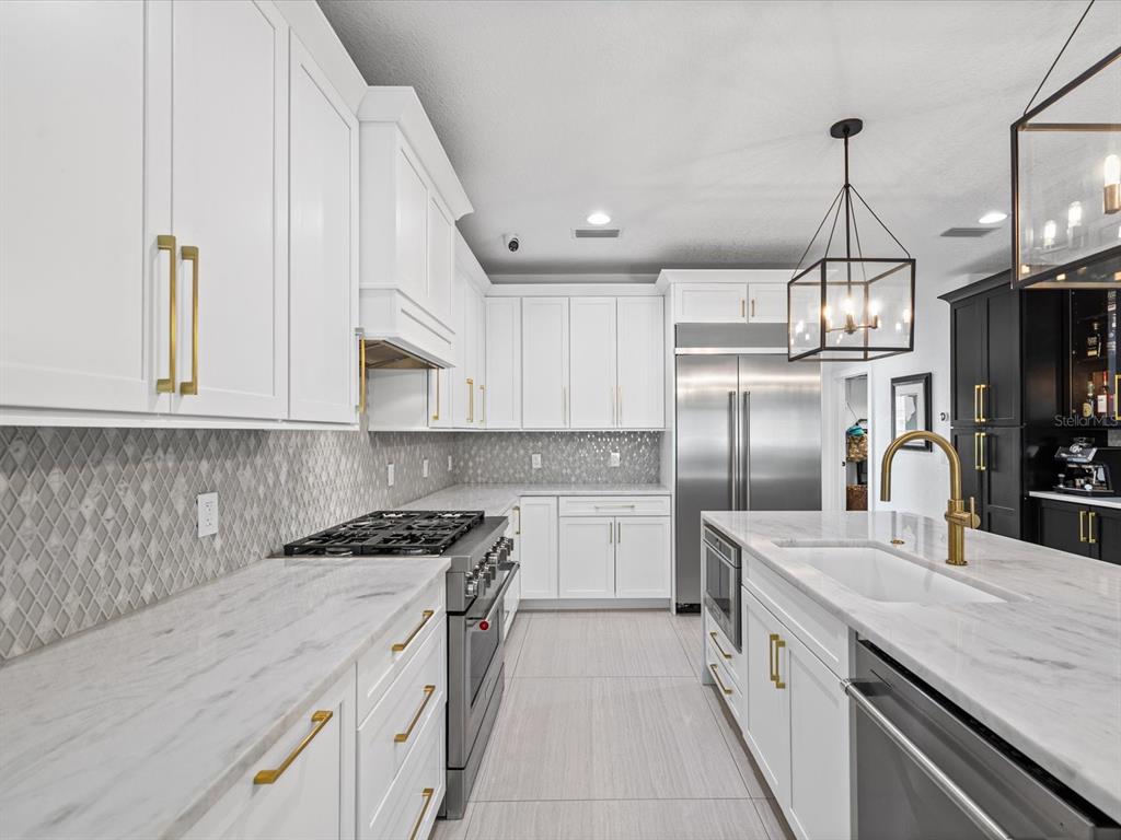 A modern kitchen features white cabinets, marble countertops, a central island, and gold hardware — 138 175TH AVENUE E, REDINGTON SHORES, FL
