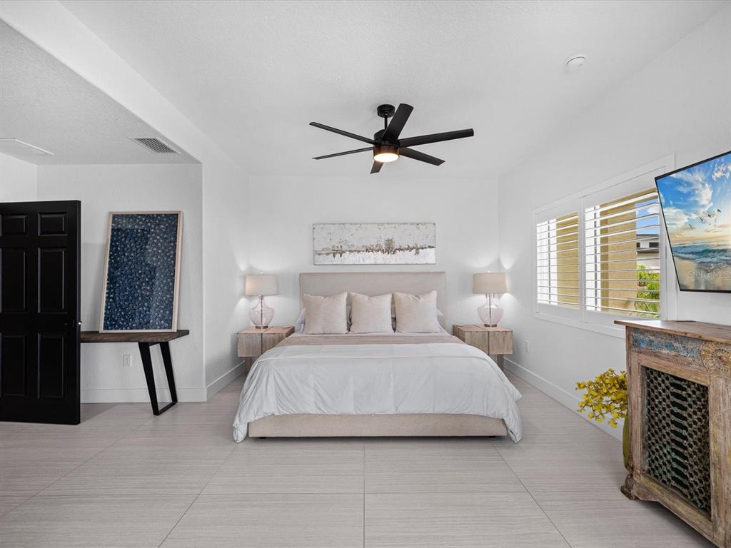 A bedroom features a bed with a beige headboard, a ceiling fan, and tile flooring — 138 175TH AVENUE E, REDINGTON SHORES, FL