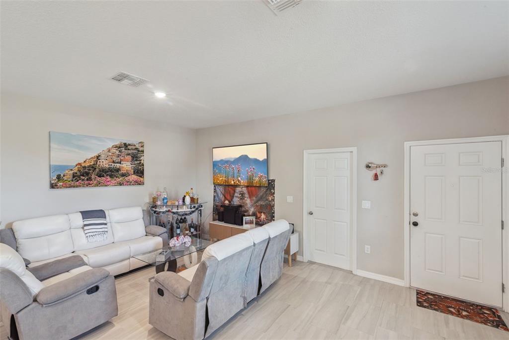 A living room features light wood-look flooring, a white sofa, a grey loveseat, and a television — 1021/1023 TITCOMB STREET, EUSTIS, FL