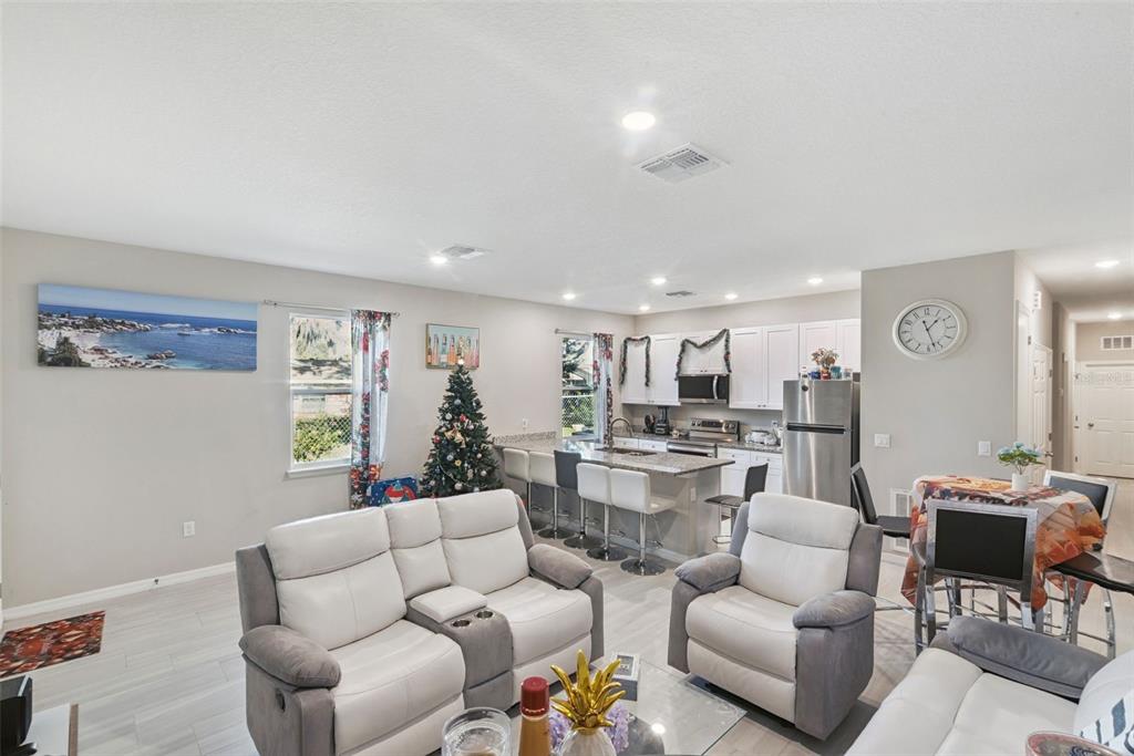 An open-concept living room and kitchen featuring white cabinetry, stainless steel appliances, and light flooring — 1021/1023 TITCOMB STREET, EUSTIS, FL