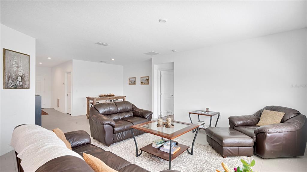 A living room features brown leather furniture, a glass-topped coffee table, and tile flooring — 285 WHITE HERON WAY, ST CLOUD, FL