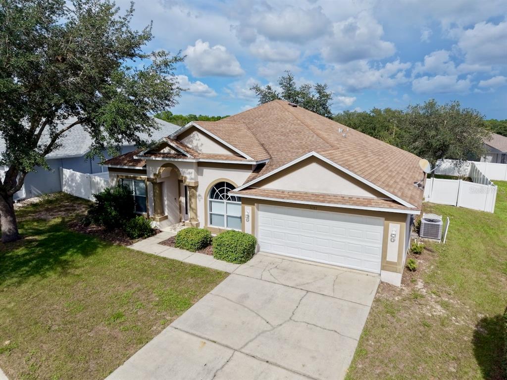 An aerial view shows a single-story house with a tan exterior, brown roof, and driveway — 5683 BRACKENWOOD DRIVE, SPRING HILL, FL