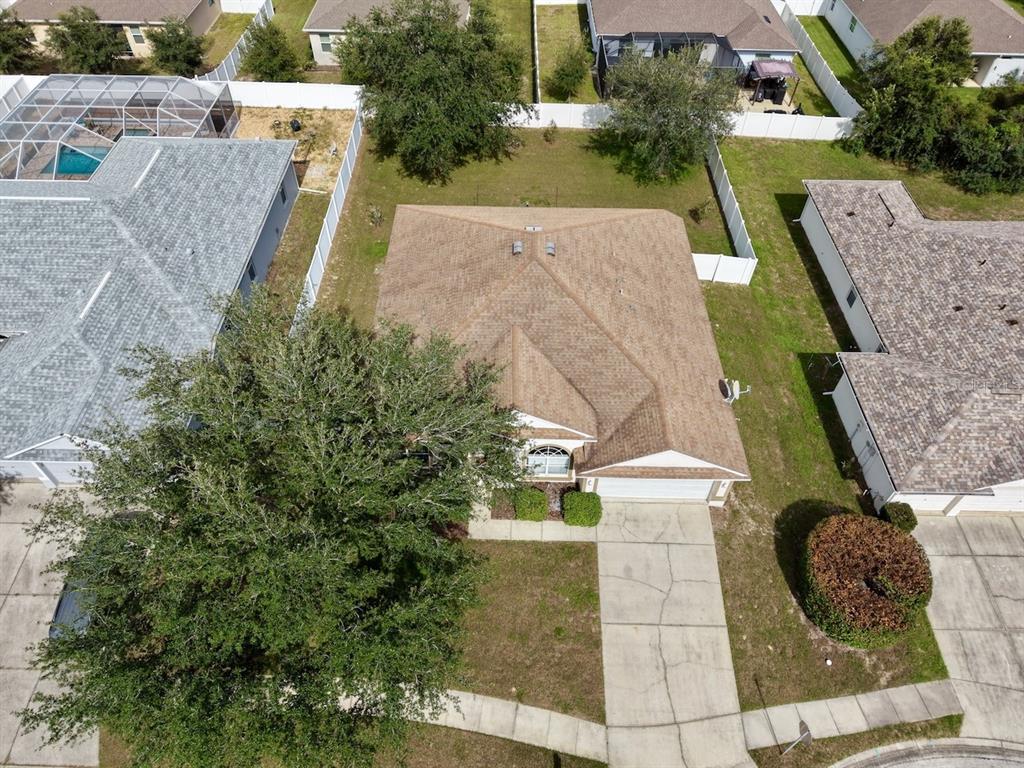 An aerial view shows a single-story house with a brown roof, driveway, and fenced backyard — 5683 BRACKENWOOD DRIVE, SPRING HILL, FL