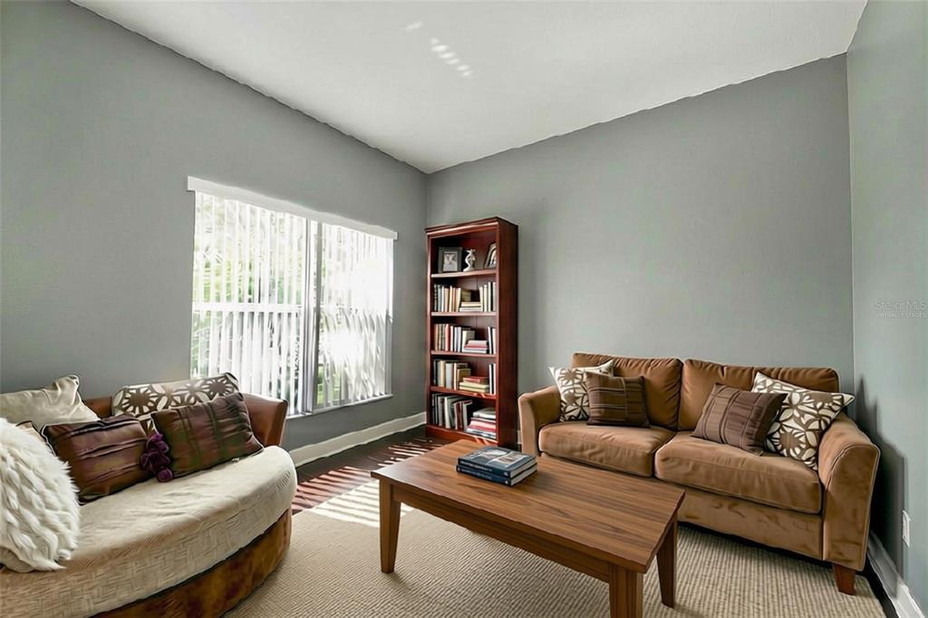 A living room features gray walls, a brown sofa, a round chair, and a bookshelf — 5683 BRACKENWOOD DRIVE, SPRING HILL, FL