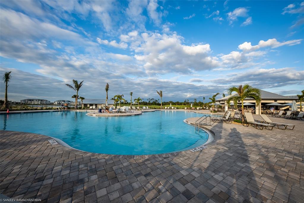 A large resort-style swimming pool with lounge chairs and palm trees under a cloudy sky — 14132 POPPY FIELD LOOP UNIT 4022, PUNTA GORDA, FL