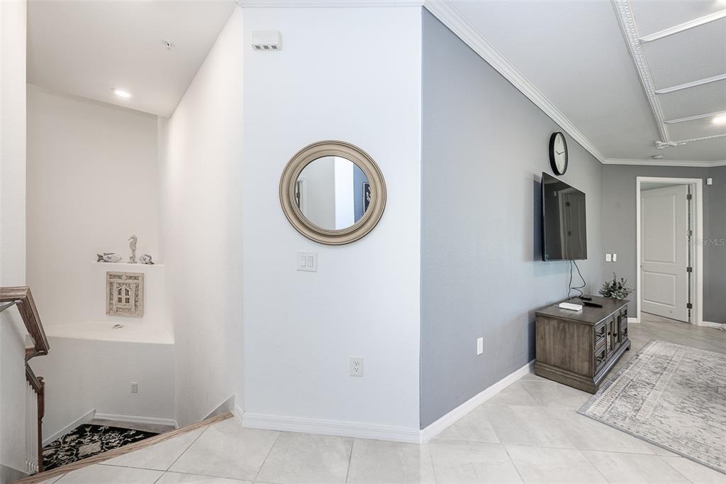 A view of a living area with a staircase, a round mirror, and a television — 14132 POPPY FIELD LOOP UNIT 4022, PUNTA GORDA, FL