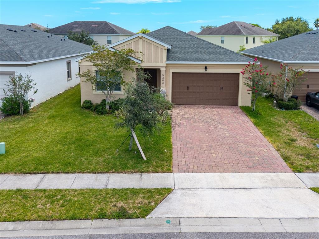A single-story suburban house features a tan stucco exterior, a brick paver driveway, and landscaping — 5303 CALADESI, PORT ORANGE, FL
