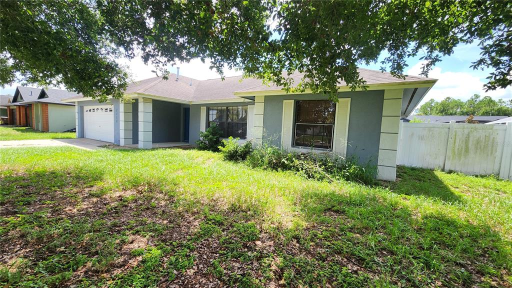 A single-story house with a gray exterior, white trim, and an overgrown front lawn — 7712 SIMON RIDGE COURT, KISSIMMEE, FL