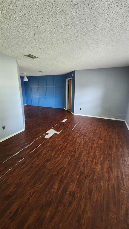An empty room features dark wood-look flooring with visible damage and a blue accent wall — 7712 SIMON RIDGE COURT, KISSIMMEE, FL