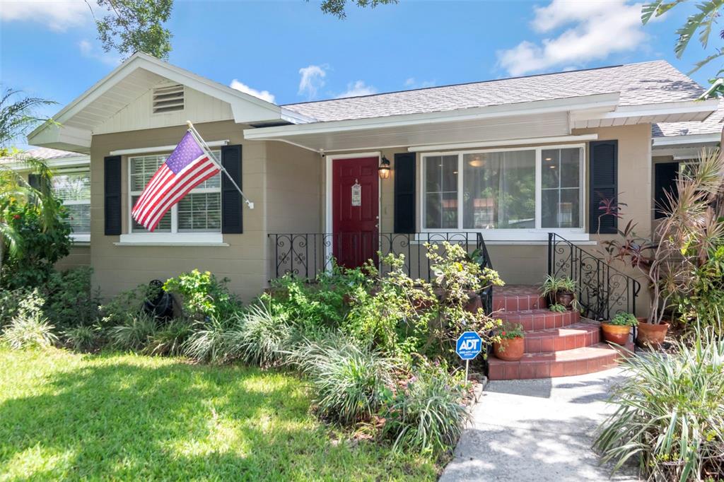 A tan single-story house with a red front door, American flag, and brick porch steps — 311 N GOMEZ AVENUE, TAMPA, FL