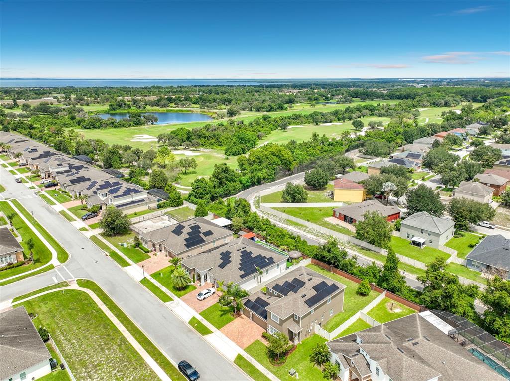 An aerial view shows a suburban neighborhood with houses featuring solar panels near a golf course — 1083 DUSTY PINE DRIVE, APOPKA, FL