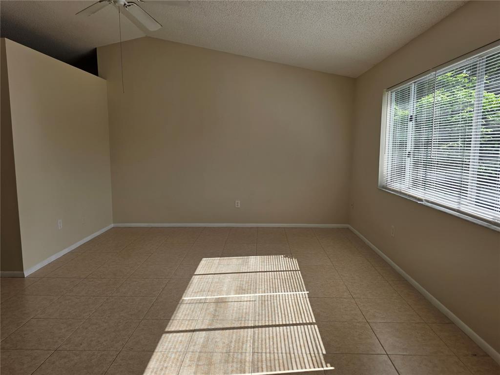 An empty room with beige tile flooring, light-colored walls, and a large window with blinds — 8507 CALADESI ISLAND DRIVE, TEMPLE TERRACE, FL