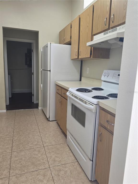 A kitchen features light wood cabinets, white appliances, and beige tile flooring — 8507 CALADESI ISLAND DRIVE, TEMPLE TERRACE, FL