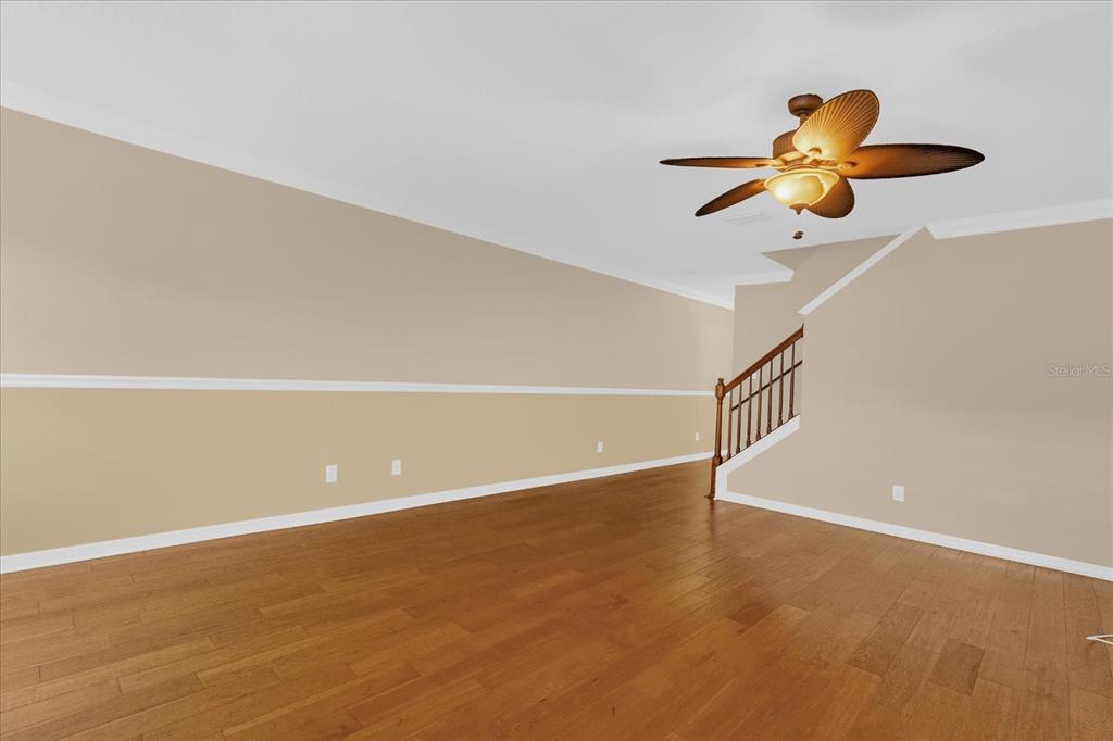 An empty room features hardwood floors, a ceiling fan, and a staircase with wooden railings — 5440 RIVER ROCK ROAD UNIT 5440, LAKELAND, FL