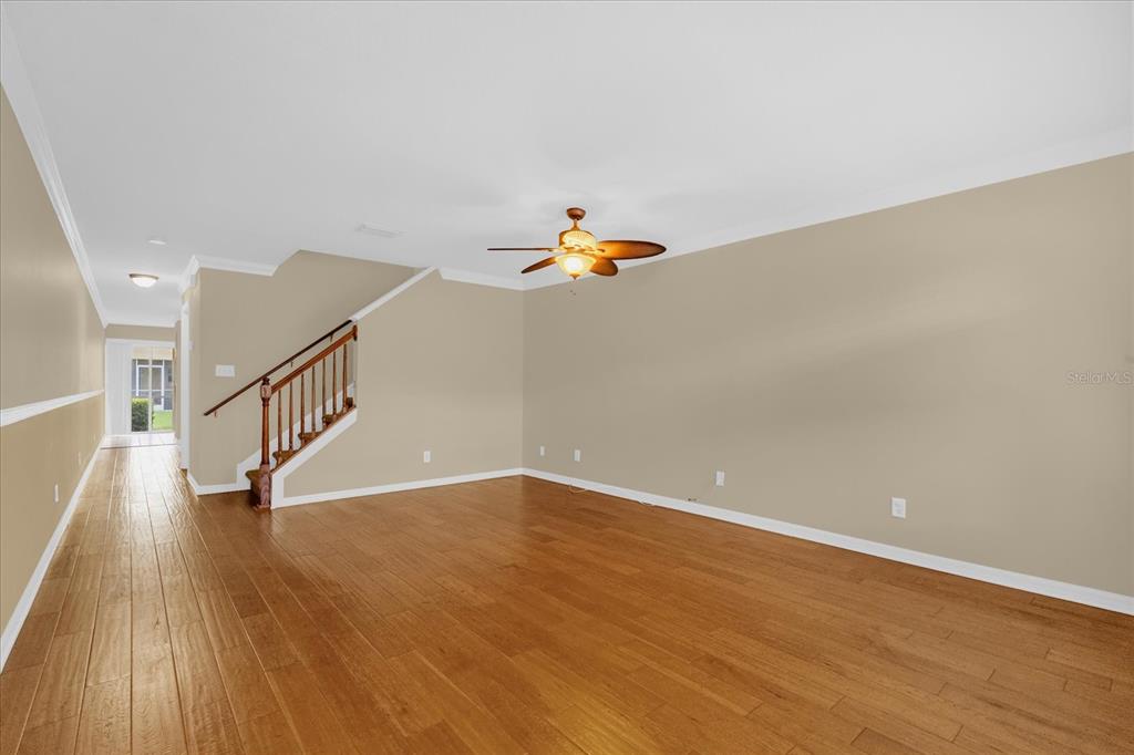 An empty living room features light-colored walls, hardwood flooring, and a wooden staircase — 5440 RIVER ROCK ROAD UNIT 5440, LAKELAND, FL