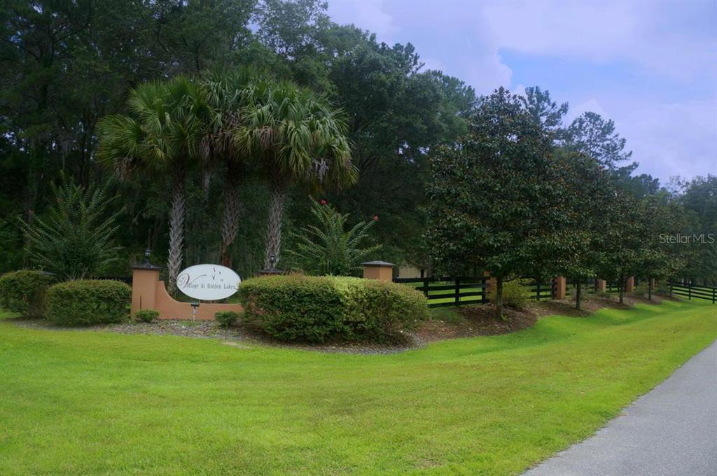 A sign for Village at Hidden Lakes stands in a landscaped yard with palm trees — TBD NW 148 LANE, WILLISTON, FL