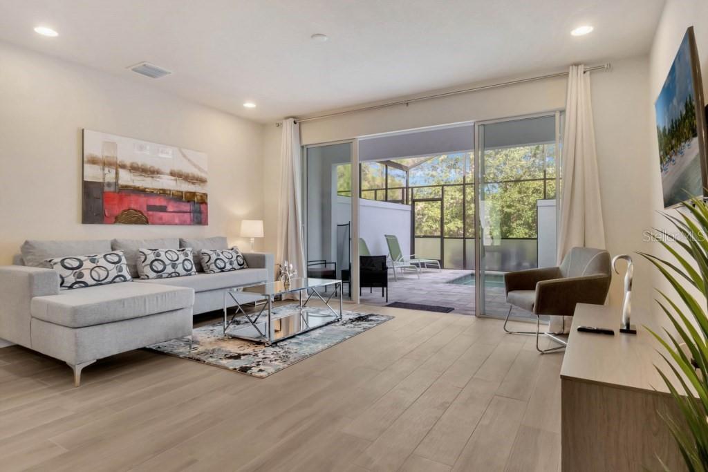 A living room with light wood floors, a grey sectional, and sliding doors to a pool — 17305 HIDDEN FOREST DRIVE, CLERMONT, FL