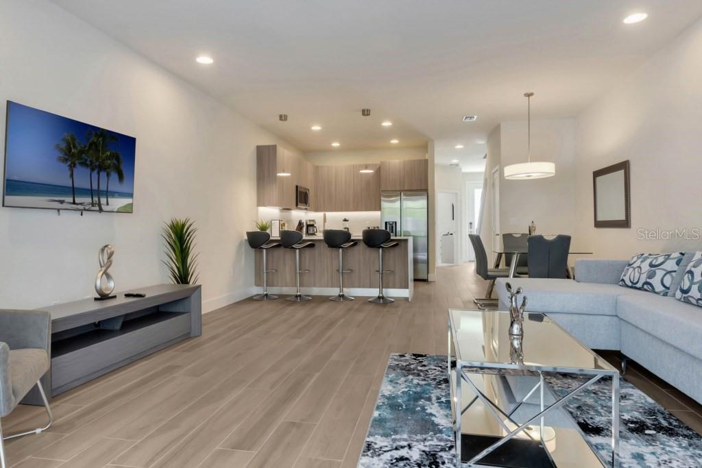 An open-concept living room and kitchen featuring wood-look flooring, bar seating, and modern decor — 17305 HIDDEN FOREST DRIVE, CLERMONT, FL