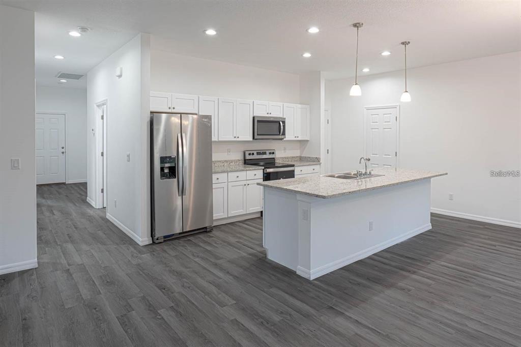 A modern kitchen features white cabinets, stainless steel appliances, a granite island, and gray flooring — 561 WILDMER ROAD SW, PALM BAY, FL