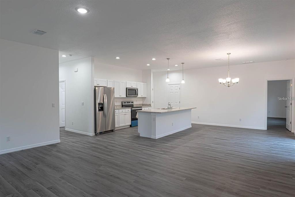 An open-concept kitchen and living area features white cabinetry, stainless steel appliances, and gray flooring — 561 WILDMER ROAD SW, PALM BAY, FL