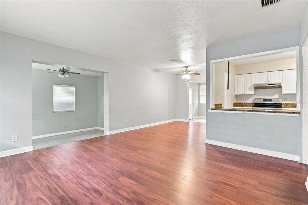 An open-concept living area with wood-look flooring, light gray walls, and a kitchen pass-through window — 3519 CALUMET DRIVE, ORLANDO, FL