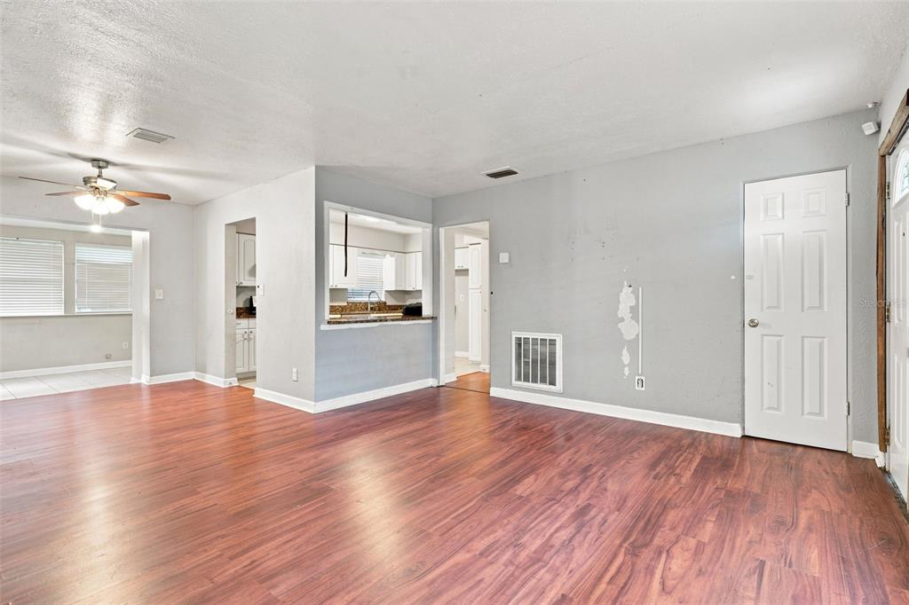 An interior view of a living room with wood-look flooring and a kitchen pass-through window — 3519 CALUMET DRIVE, ORLANDO, FL