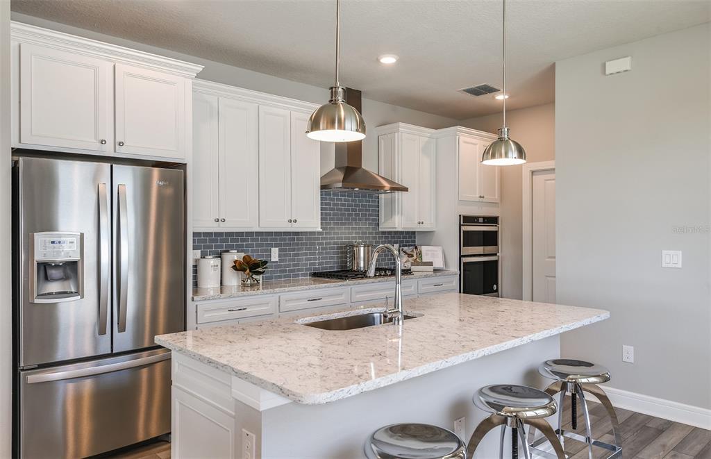 A kitchen features white cabinets, a granite island, stainless steel appliances, and a gray backsplash — 15029 SUNBEAM STREET, PARRISH, FL