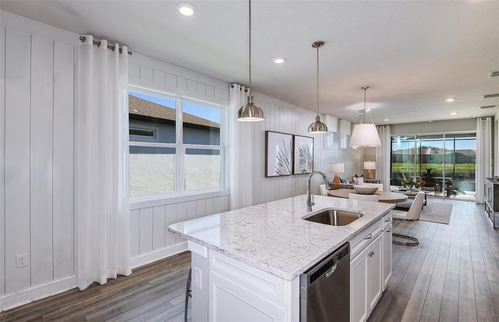 A kitchen island with a sink and stone countertop sits before a dining area — 15029 SUNBEAM STREET, PARRISH, FL