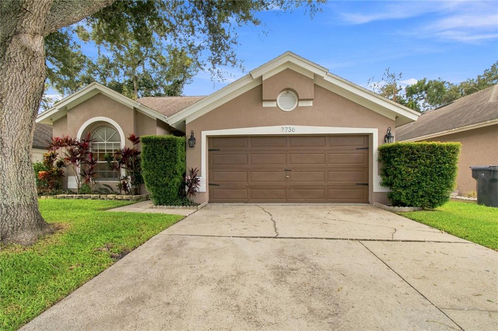 A single-story house with a brown garage door, beige stucco exterior, and a concrete driveway — 7736 MARBELLA CREEK AVENUE, TAMPA, FL