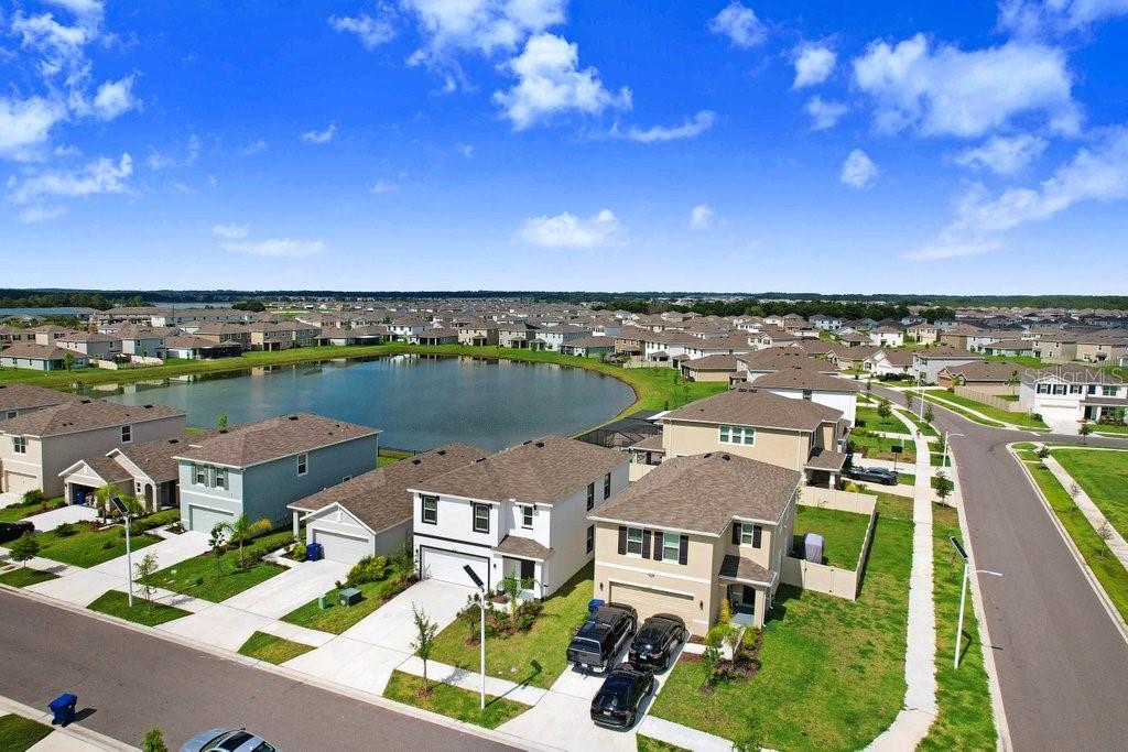 An aerial view shows suburban houses surrounding a central pond under a blue sky — 9319 FORGE BREEZE LOOP, WESLEY CHAPEL, FL