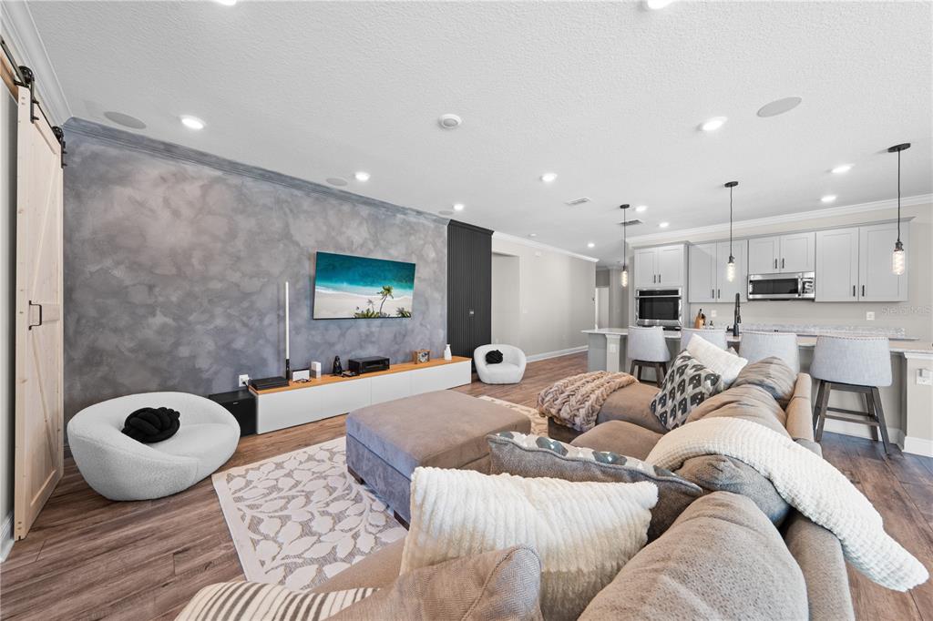 A living room with a textured gray accent wall, television, and an open-concept kitchen — 31041 JAZZ LEAF PLACE, SAN ANTONIO, FL