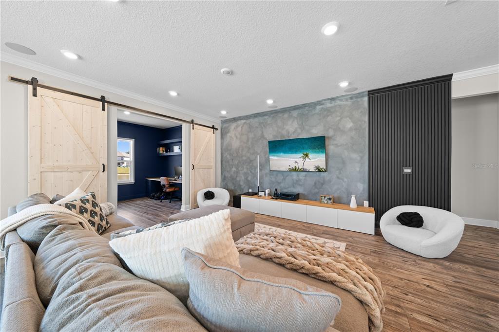A living room features a textured gray accent wall, black slat paneling, and sliding barn doors — 31041 JAZZ LEAF PLACE, SAN ANTONIO, FL