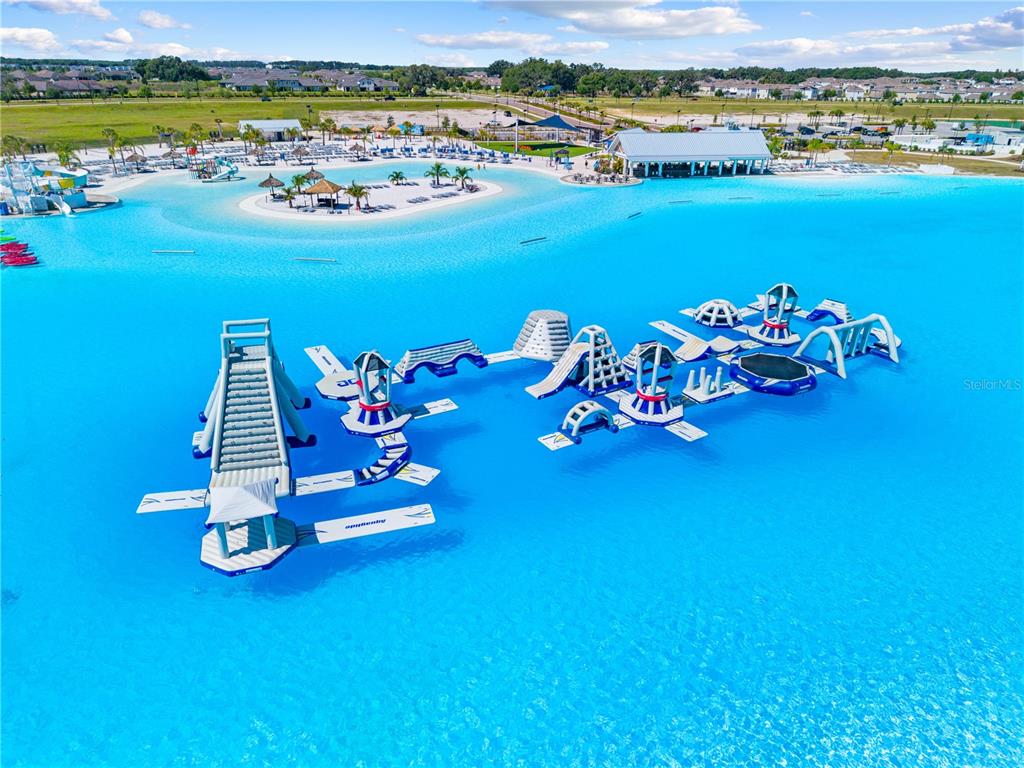An aerial view shows a large blue lagoon with an inflatable obstacle course and beach — 31041 JAZZ LEAF PLACE, SAN ANTONIO, FL